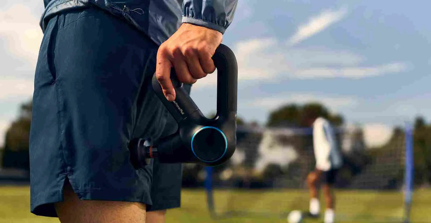 Man using a massage gun on his leg on a football field