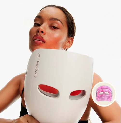 Woman using a white LED Mask with red lights on a plain background